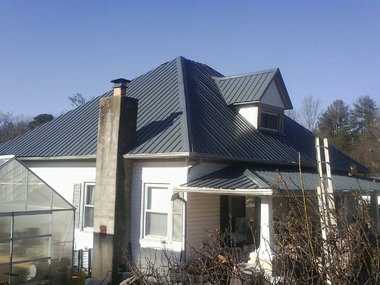 Dark blue standing seam metal roof on a white farmhouse with dormer — Slate & Tile Roof Repair by Roofing Brothers in Eyota