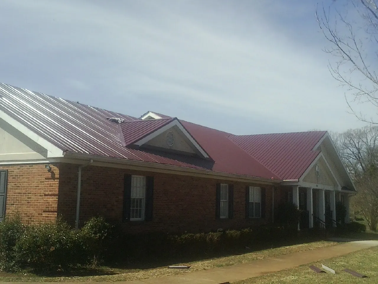 Red metal roof with gabled entries on a long brick building, from a Hail Damage Roof Repair job in Eyota
