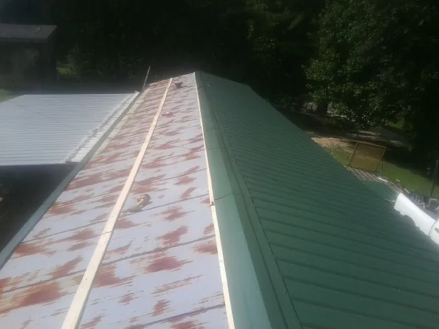 Old rusted panels beside newly installed green metal roofing — Wind Damage Roof Repair by Roofing Brothers in Eyota