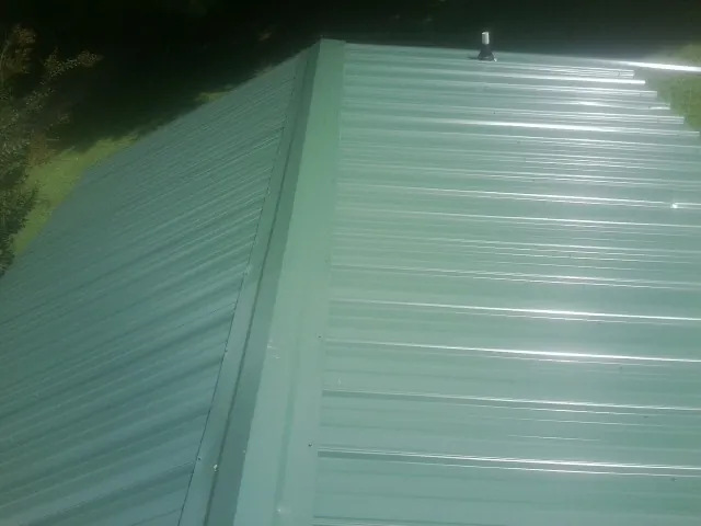 New green metal panels meeting at the ridge of a roof — Flat Roof Repair work by our crew in Eyota