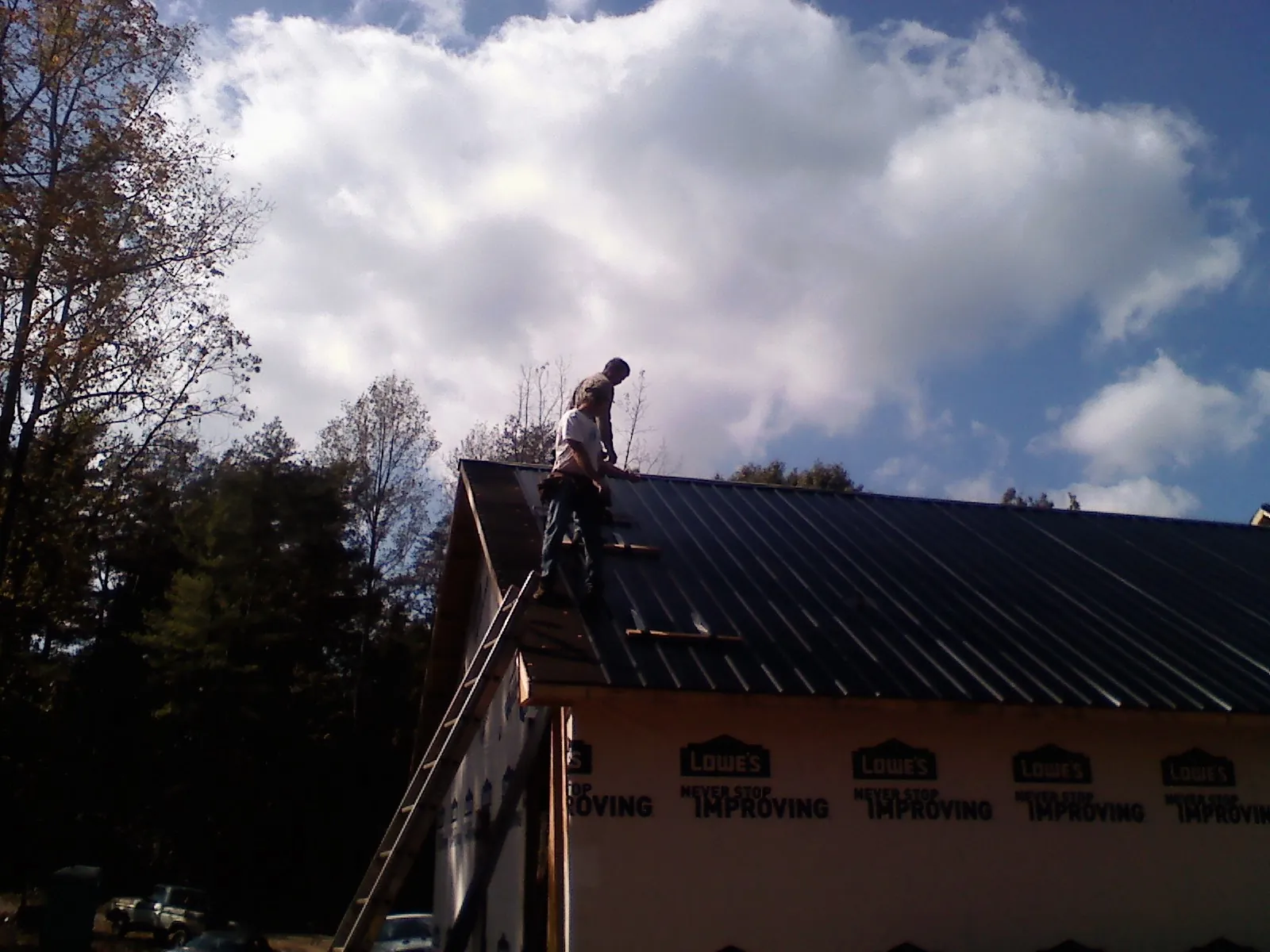 Roofer fastening dark metal panels high against a cloudy sky, from a Roof Inspection job in Eyota