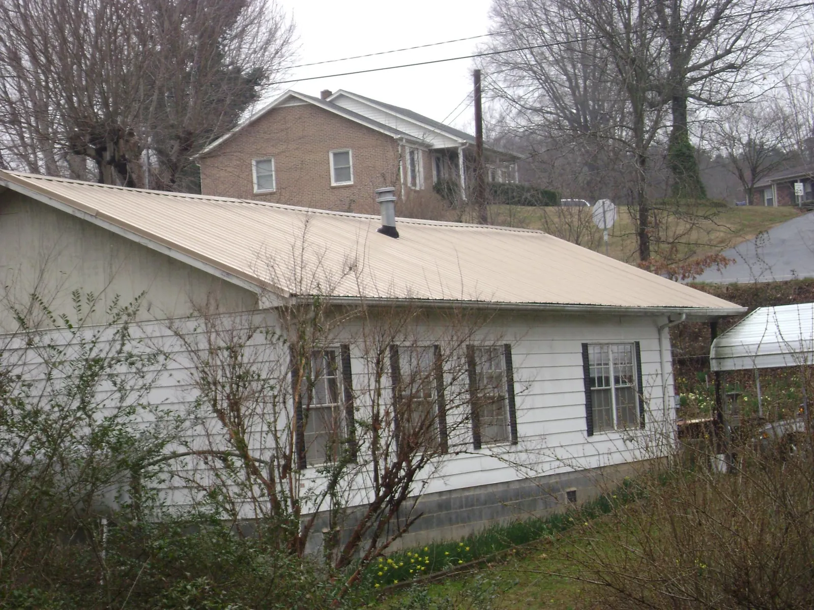 Tan metal roof on a white sided house set into a hillside — Commercial Roofing by Roofing Brothers in Eyota