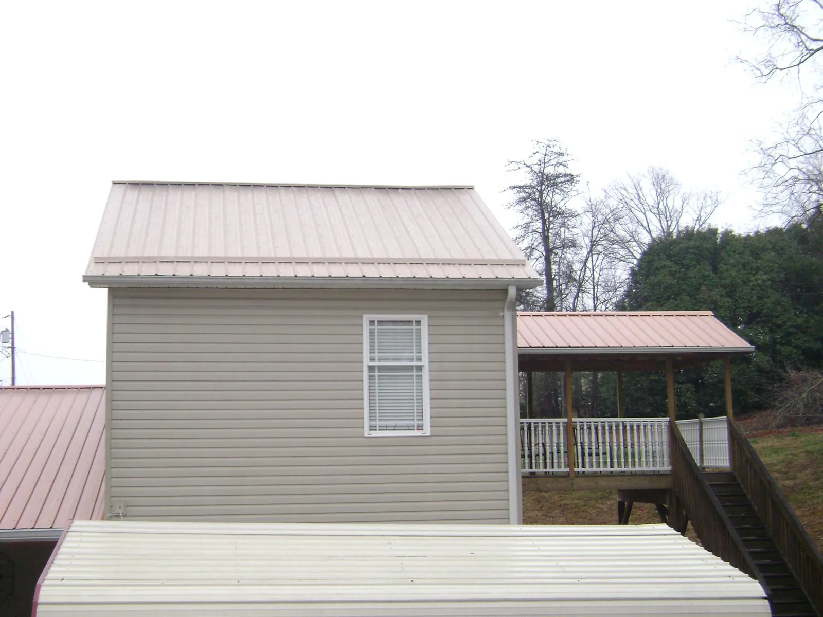 Tan metal roofs on a two story addition and attached porch, from a Roof Replacement job in Eyota